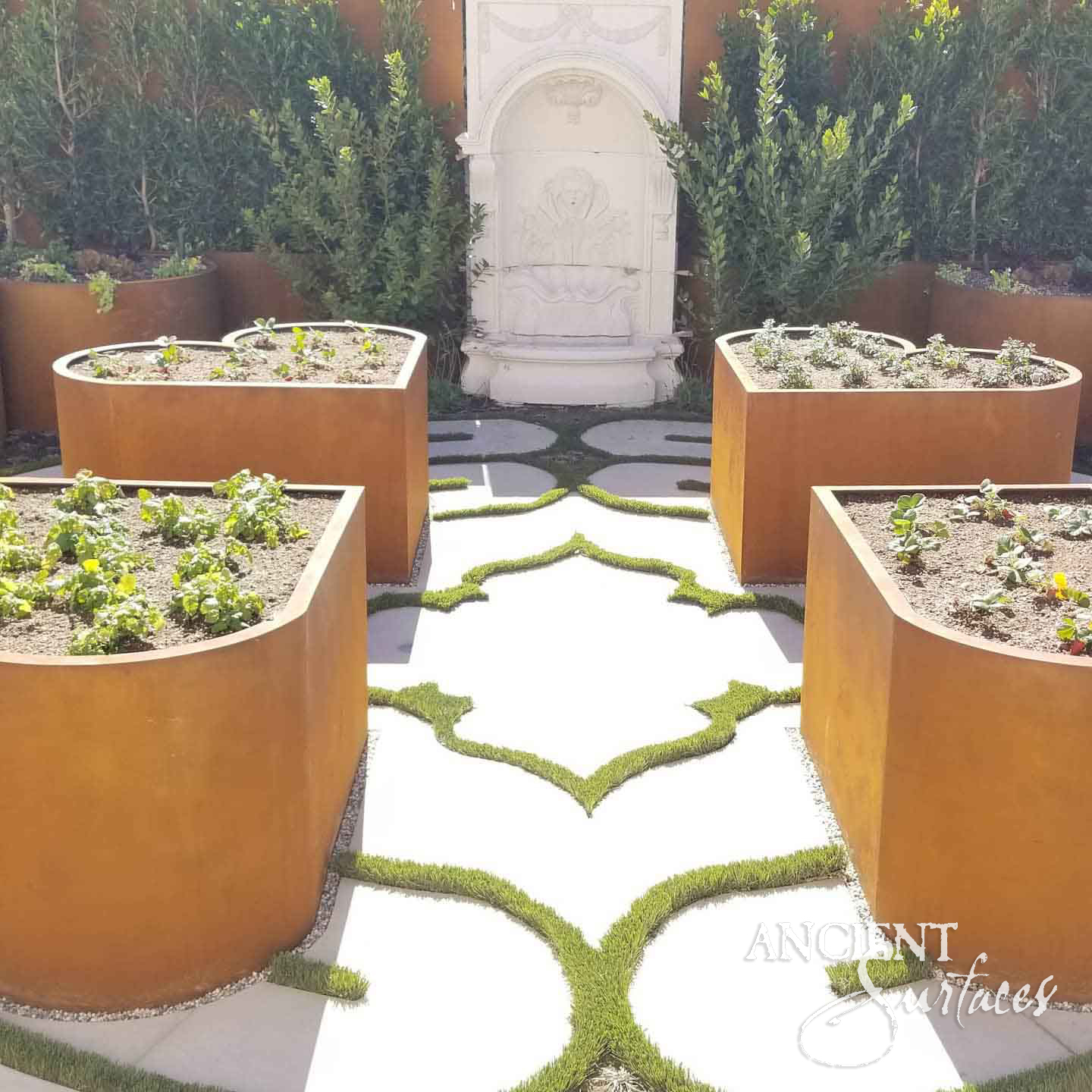 White limestone wall fountain closing the axis of a formal garden with corten planters